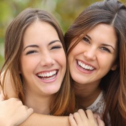 Two women friends laughing with a perfect white teeth with a green background