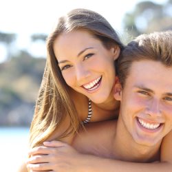 Happy couple with perfect smile and white teeth posing on the beach looking at camera